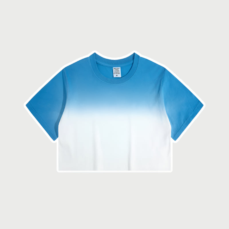 Blue and white ombré cropped short-sleeve t-shirt with gradual color fade from deep blue to white, featuring a crew neck and a small branded tag at the collar