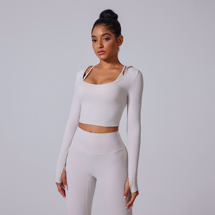 A model wearing light cream workout set with square neck long-sleeve crop top featuring shoulder cutouts and high-waisted leggings on white platform shoes