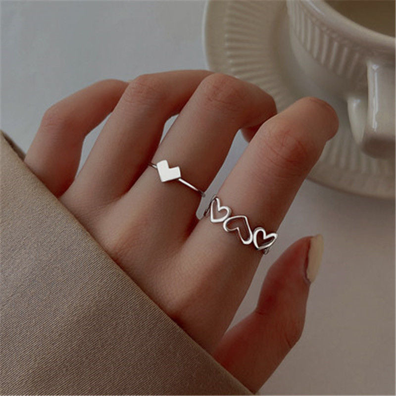 Two silver rings worn together: single heart and connected hearts band, styled with beige fabric