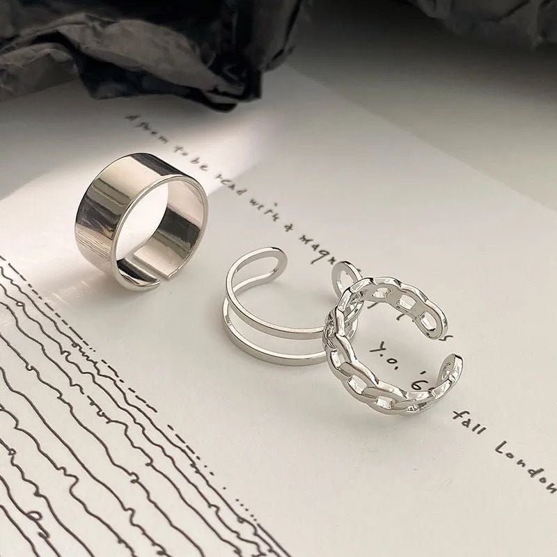 Three silver adjustable rings displayed on white paper with handwritten text, featuring polished band, double wire, and chain designs