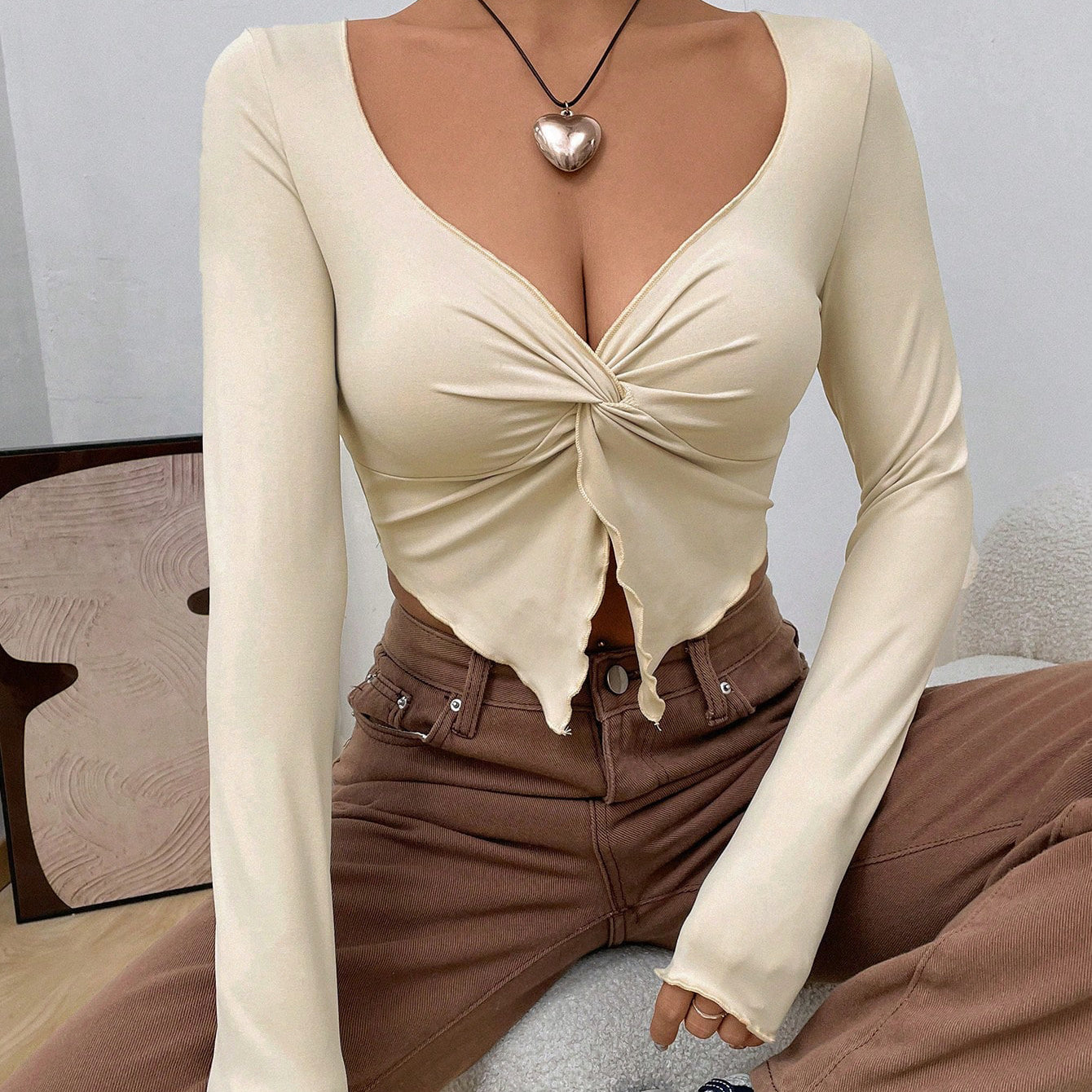 Model wearing cream long-sleeve twist-front crop top with brown jeans, silver heart necklace, and white sneakers