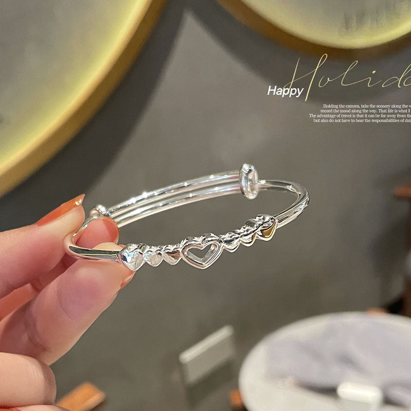 A person holding a silver heart charm bangle bracelet with multiple small hearts and adjustable closure against a holiday-themed background