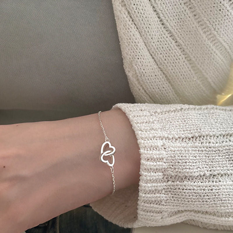 Delicate silver double heart bracelet on wrist, paired with cream knit sweater sleeve
