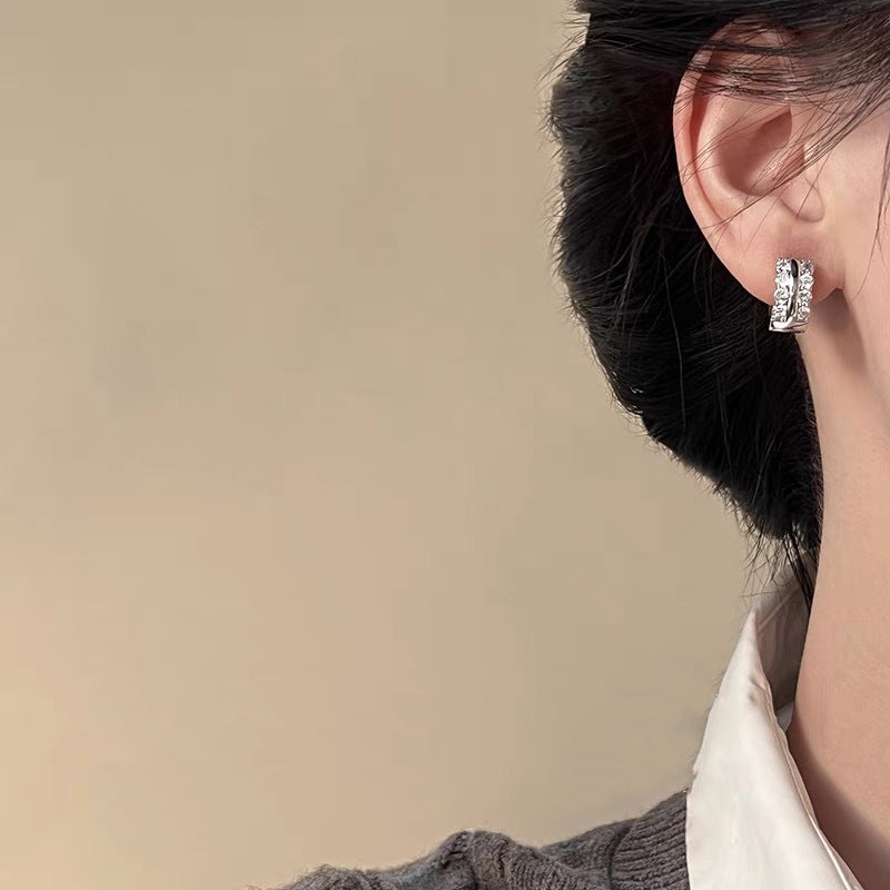 Small silver huggie hoop earring with double row of crystals worn on ear, neutral background
