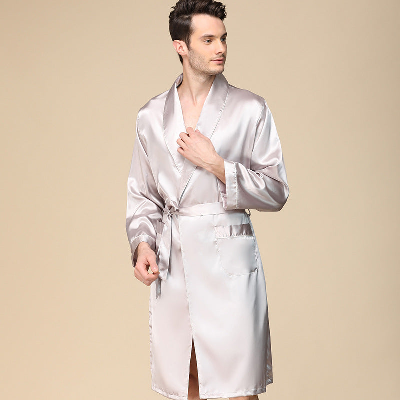 Man wearing light silver silk robe with shawl collar, tied belt and front pocket against beige background