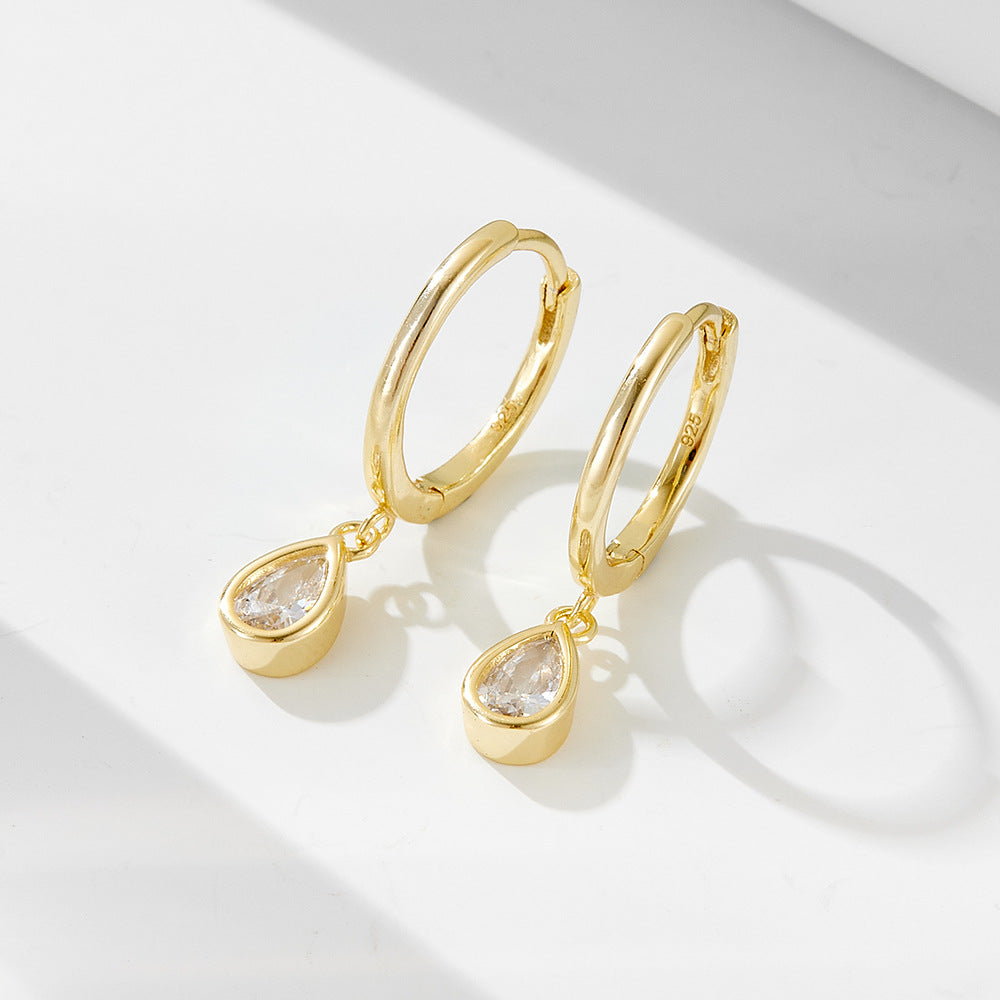 Gold huggie hoop earrings with teardrop crystal charms displayed on white surface with soft shadows
