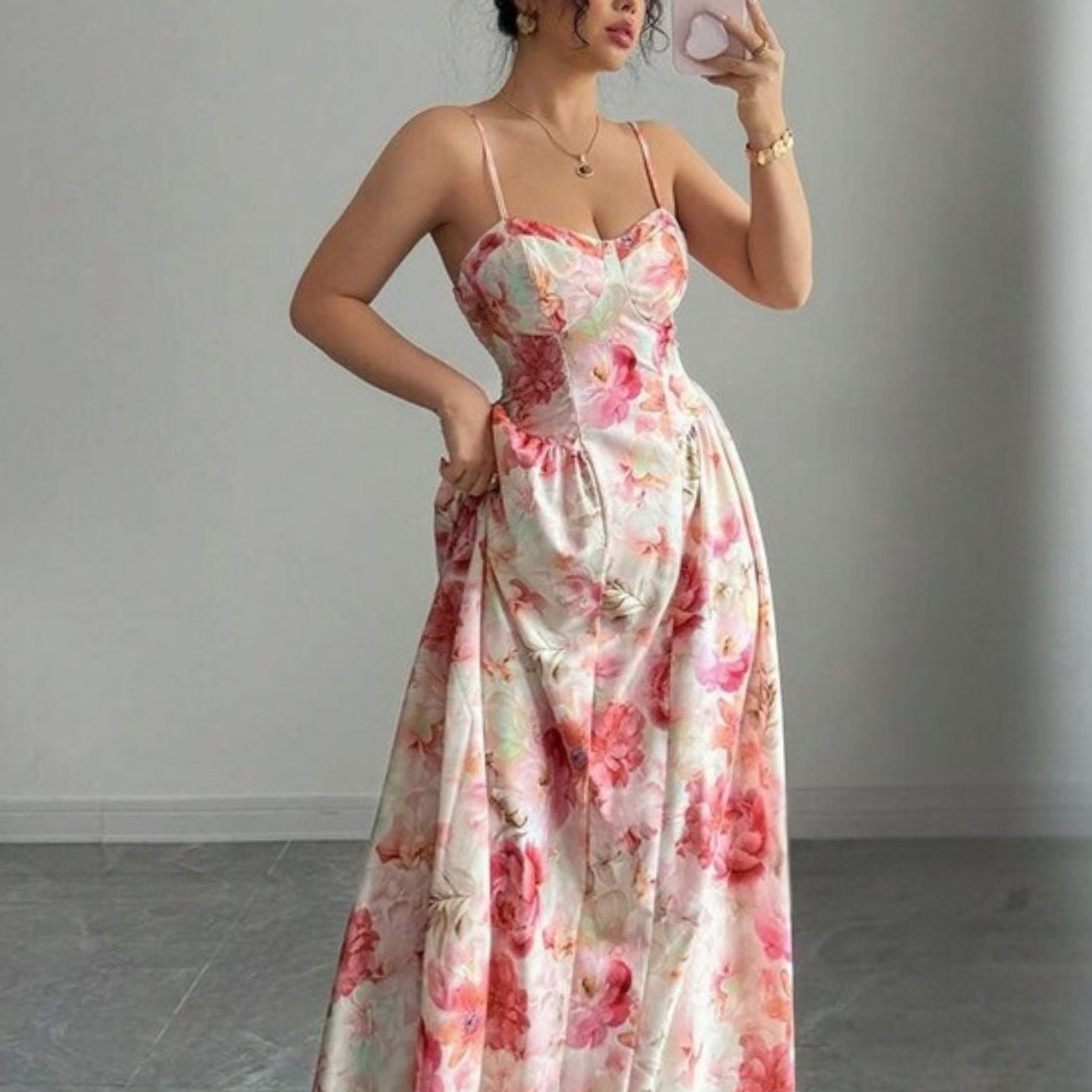Woman taking a mirror selfie wearing a floral dress in a minimalistic setting.