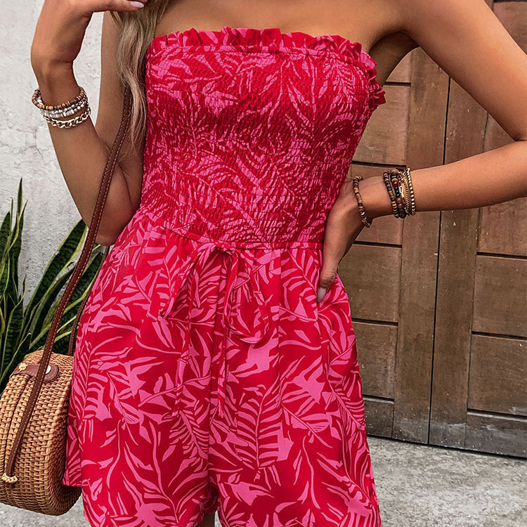 Close-up of a woman in a red off-shoulder romper with a ruched top and tropical print, posing with hand on hip.