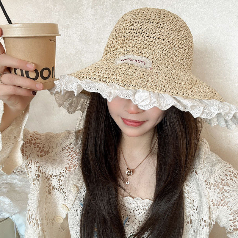 Woman in a beige woven straw hat with white lace trim, holding a takeaway coffee cup, smiling softly in a lace cardigan.