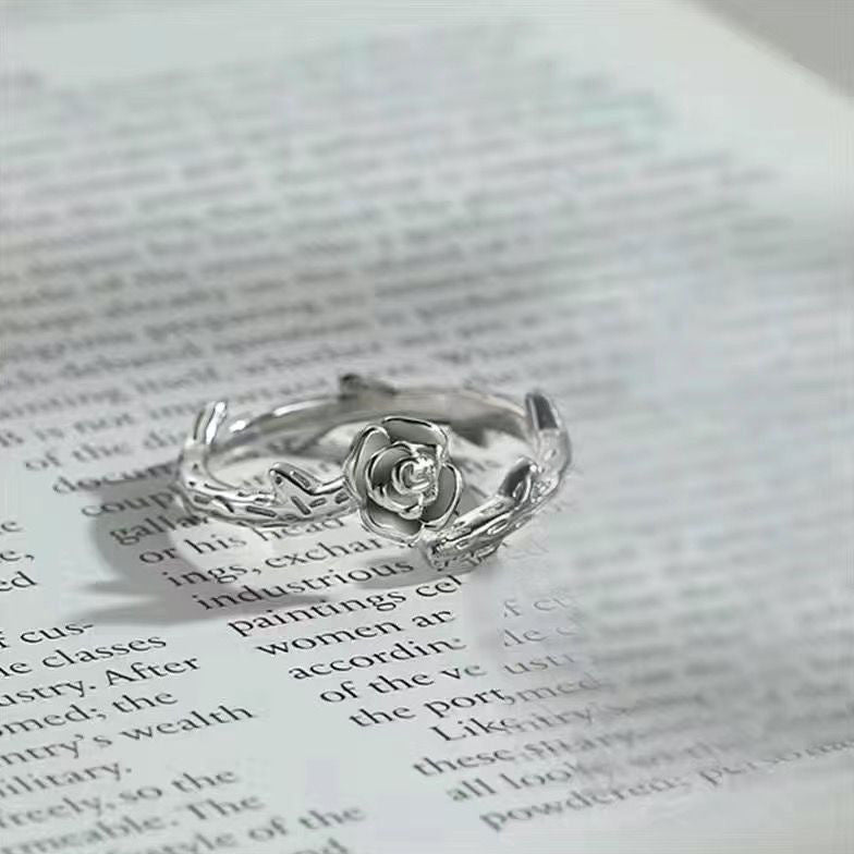 A delicate silver ring featuring a rose blossom with twig-like band resting on a printed book page, photographed in close-up