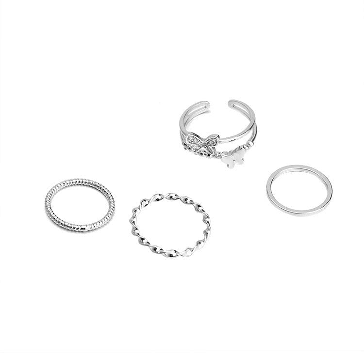 Four silver rings laid out flat, including a butterfly-themed ring with layered bands and three minimalist textured and plain band rings