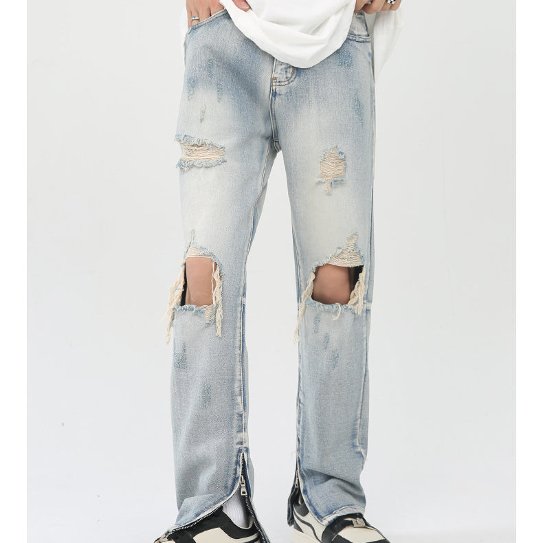 Model wearing light wash distressed jeans with knee rips, ankle zips, white tee and black/white sneakers on white backdrop
