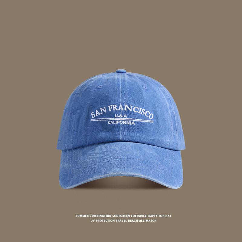 A blue washed denim baseball cap with white 'San Francisco USA California' embroidery displayed against taupe background with UV protection text