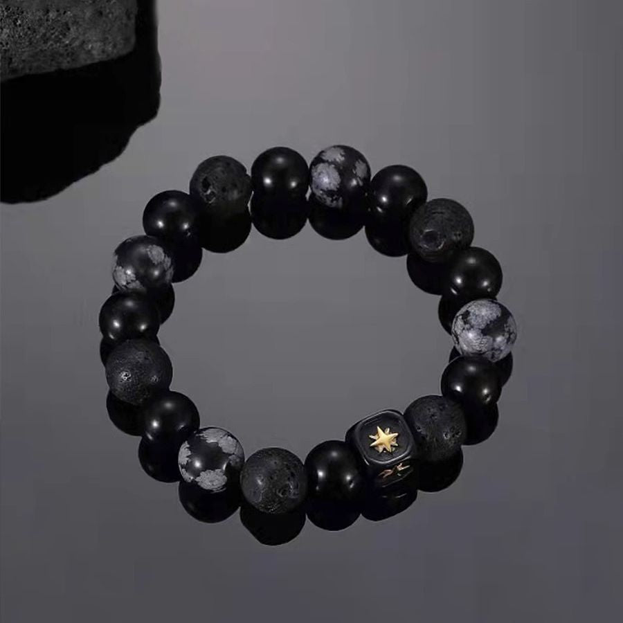 Black beaded bracelet with obsidian, lava stone and marble finish beads featuring gold star charm on dark background