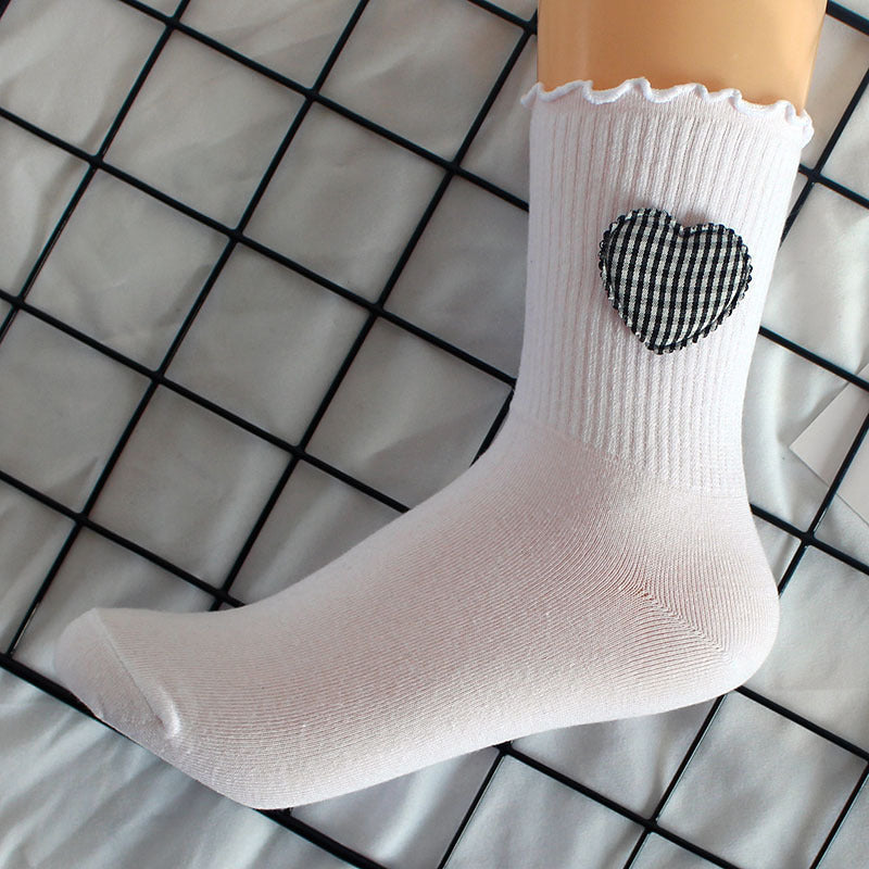 White crew sock with ruffle trim and gingham heart patch against grid background