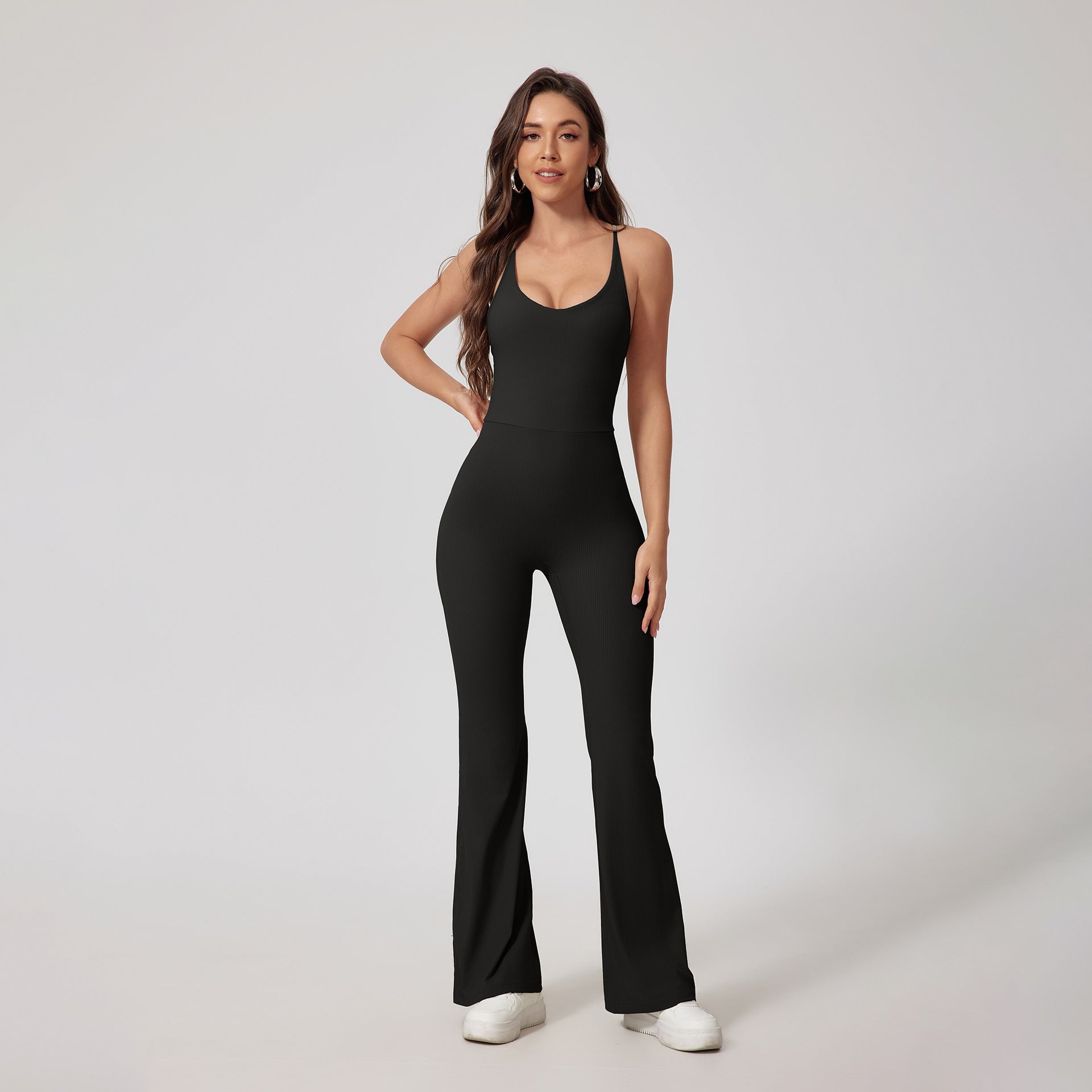 Woman in black fitted flared jumpsuit with halter neckline, paired with white platform sneakers