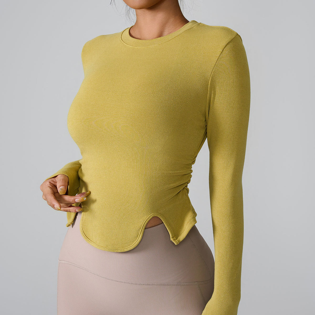 Close-up of mustard yellow long sleeve top showing ruched side detail and curved cutout hem design, professional product shot