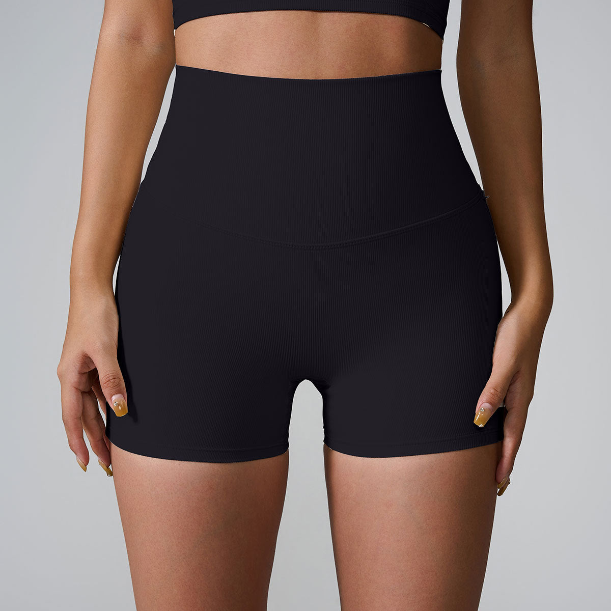 A model wearing black high-waisted ribbed compression shorts and matching sports bra, studio lighting on gray background
