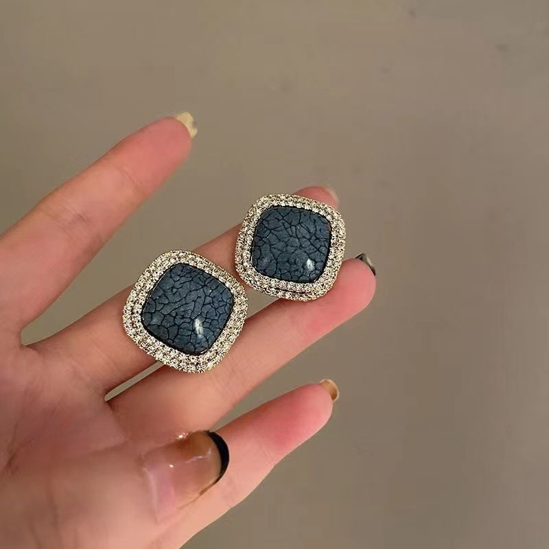 Pair of navy blue crackle stone earrings with crystal borders displayed on palm