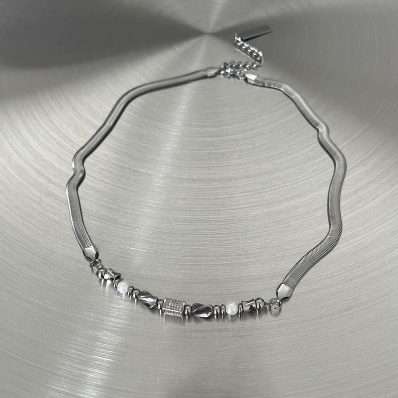 Silver necklace with varied beads and smooth chain on brushed surface.
