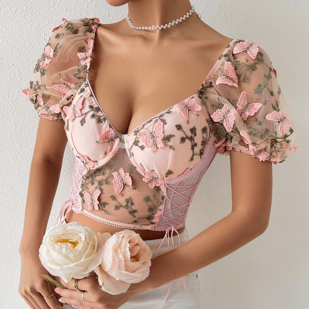 Woman in a light pink butterfly mesh crop top with lace-up sides and puff sleeves.
