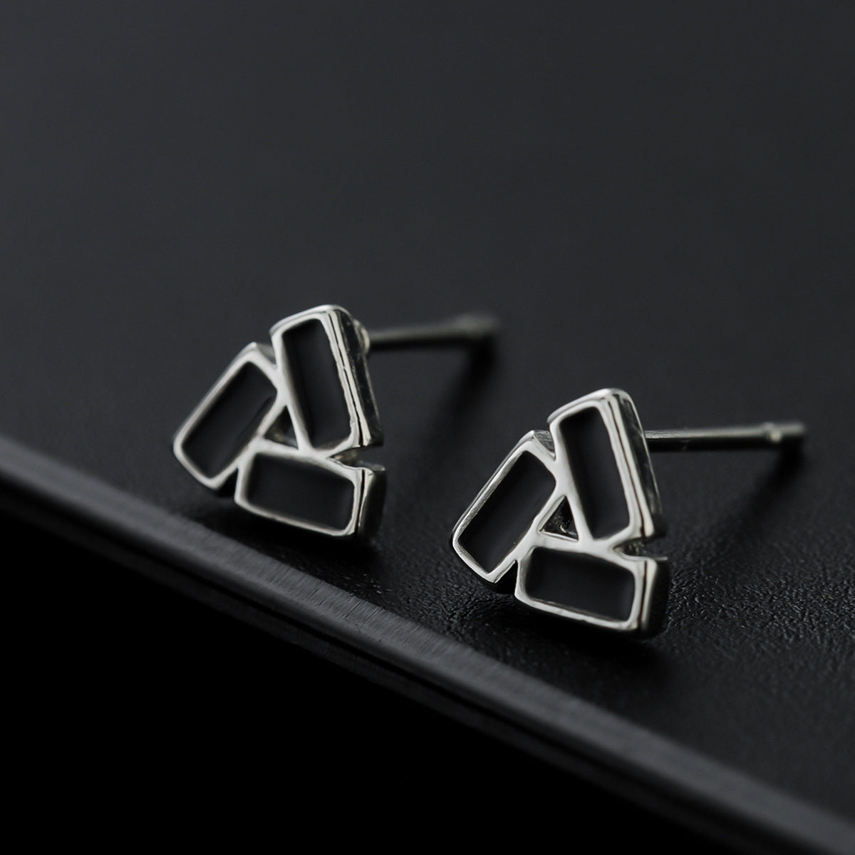Close-up of geometric stud earrings on matte black edge.