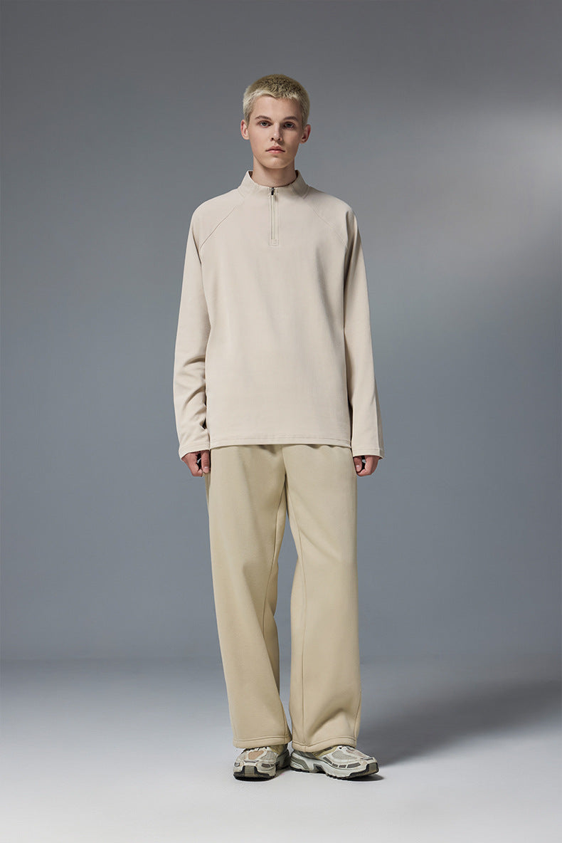 Person wearing a khaki half zip long sleeve t shirt styled with beige pants on a gray background