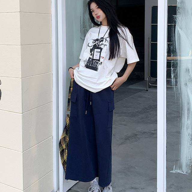 Model poses at doorway in navy maxi skirt with cargo pockets, graphic tee, and chunky sneakers.