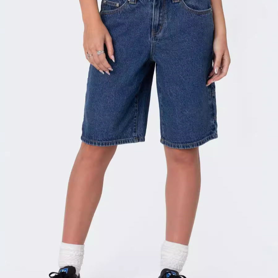 Front view of woman wearing plain dark wash knee-length denim shorts paired with black sneakers and white socks.