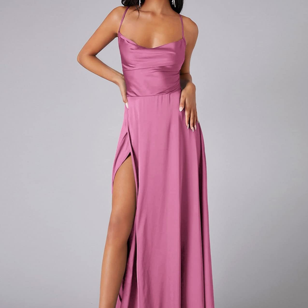 Woman wearing a pink evening gown with a high slit on a gray background