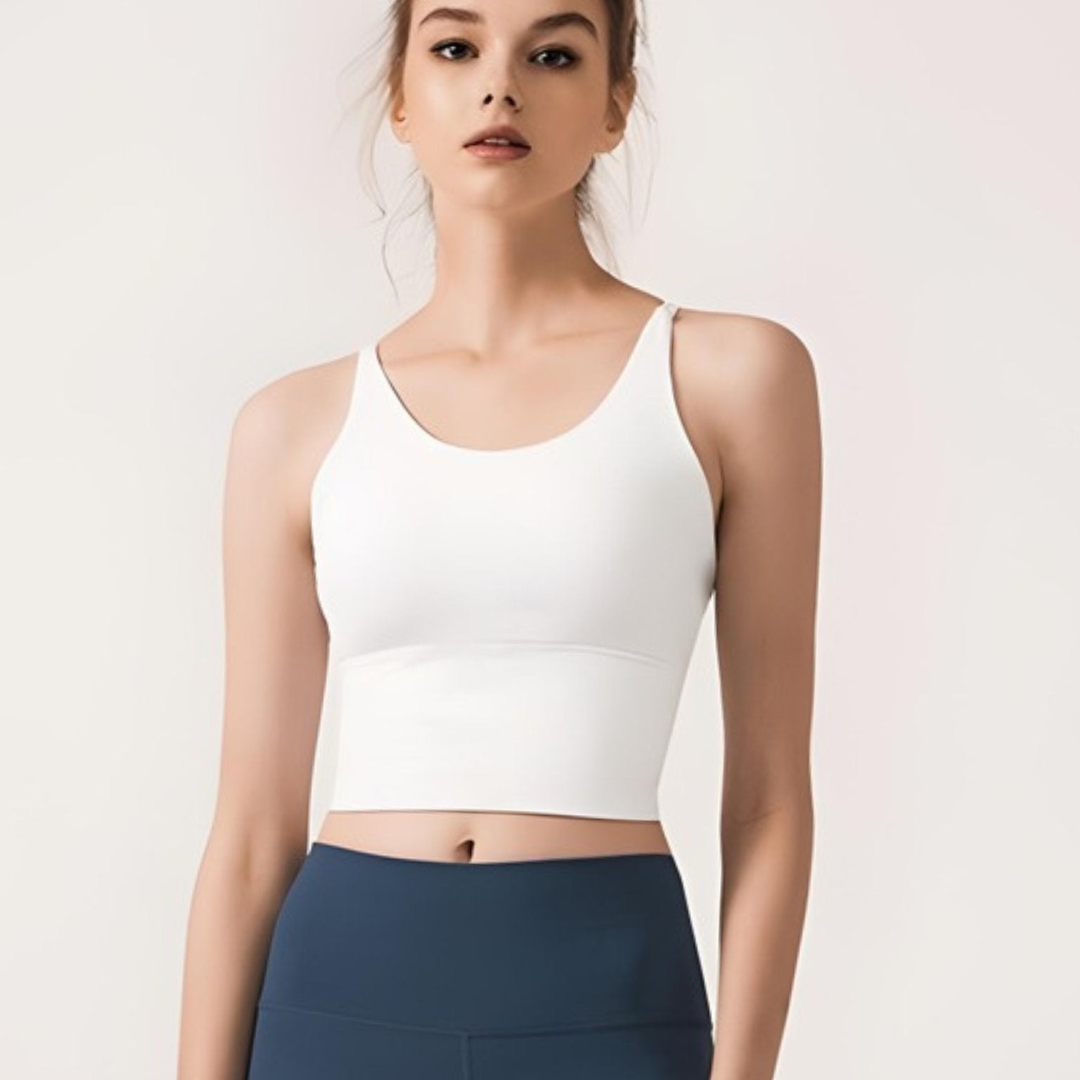 Woman models front view of white strappy yoga sports bra.