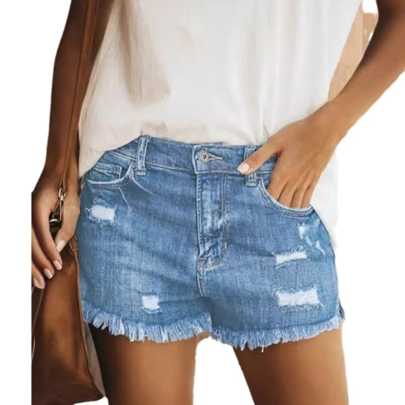 Woman wearing light blue ripped denim shorts with raw hems and a loose white top outdoors.