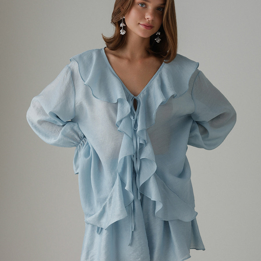 Woman wearing a light blue ruffled blouse set against a gray background