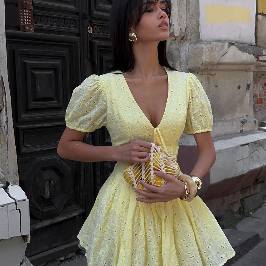 Woman in a yellow dress standing on a street with a textured wall background