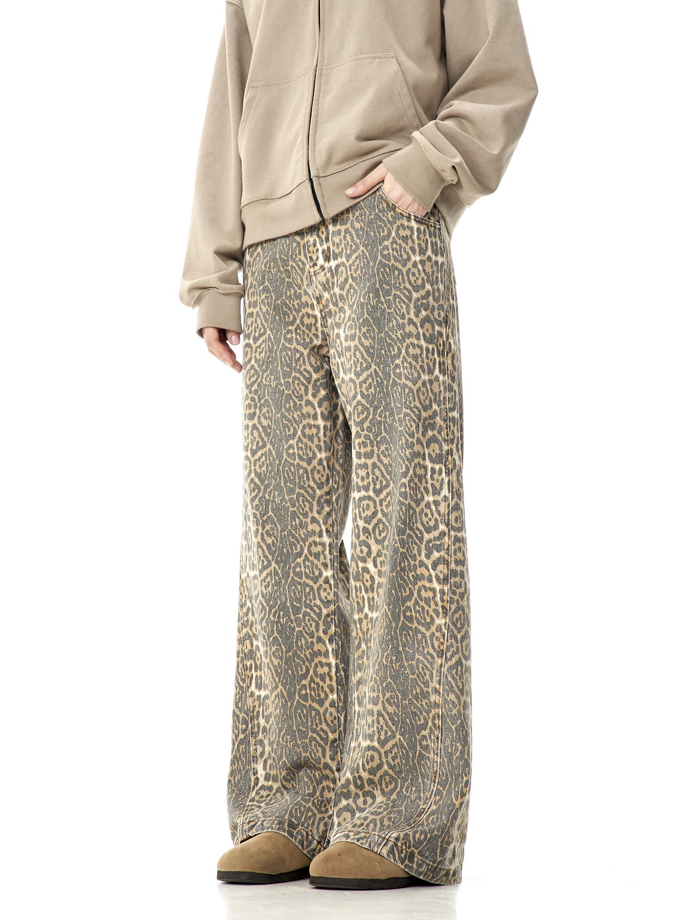 A model wearing beige zip-up hoodie and leopard print wide-leg pants with hands in pockets, standing against white background