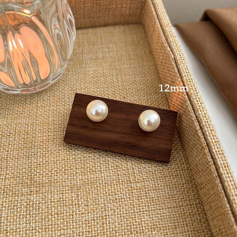 12mm pearl stud earrings displayed on wooden holder against textured burlap fabric background