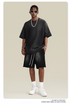 Model with short locs wearing black t-shirt and shorts set with white sunglasses, silver chain necklace and white sneakers against cream background