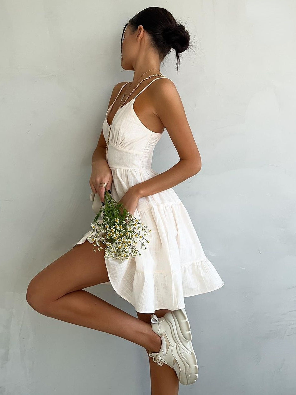 White cotton sundress with tiered skirt, spaghetti straps, and fitted bodice, styled with quilted mini bag and delicate floral accessories