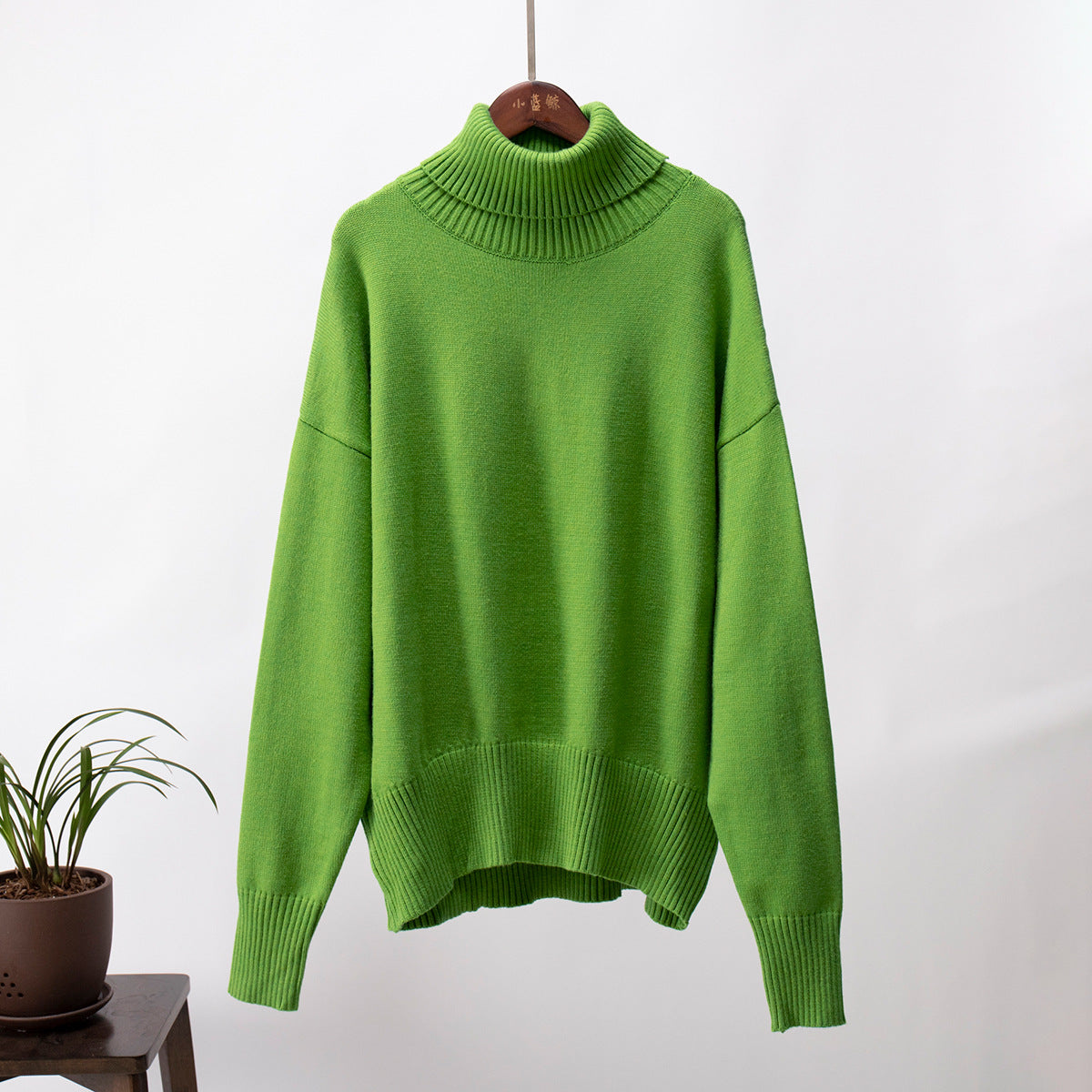 Emerald green turtleneck sweater hanging, soft knit texture, studio product shot