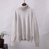 Soft white turtleneck sweater with ribbed collar, hanging on wooden hanger with minimalist backdrop