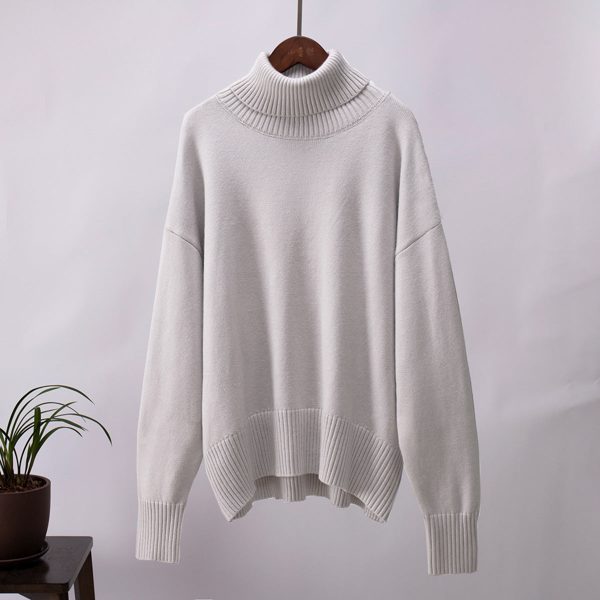 Soft white turtleneck sweater with ribbed collar, hanging on wooden hanger with minimalist backdrop
