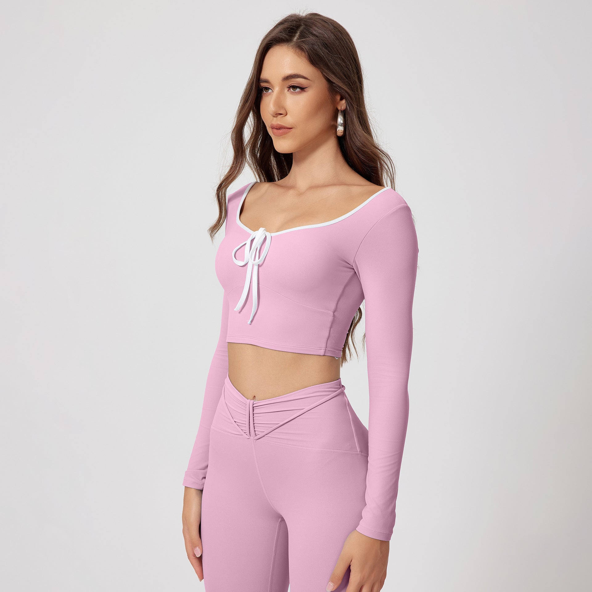 Soft pink athletic two-piece set with scoop neck crop top, front tie detail, white trim and high-waisted leggings with ruched waistband detail