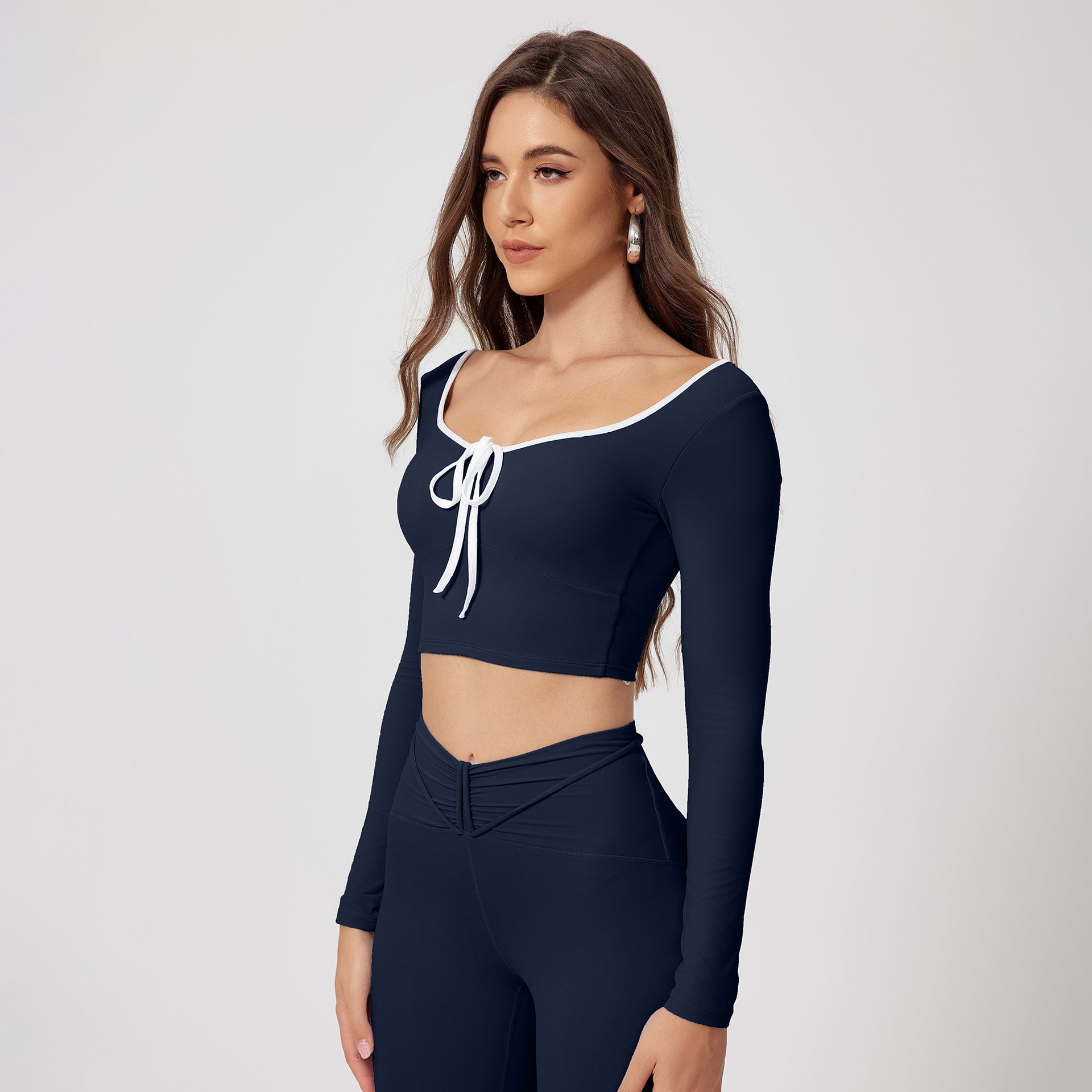 Navy blue workout set with scoop neck long sleeve crop top, decorative white tie front and matching high-waisted athletic leggings with ruched detail