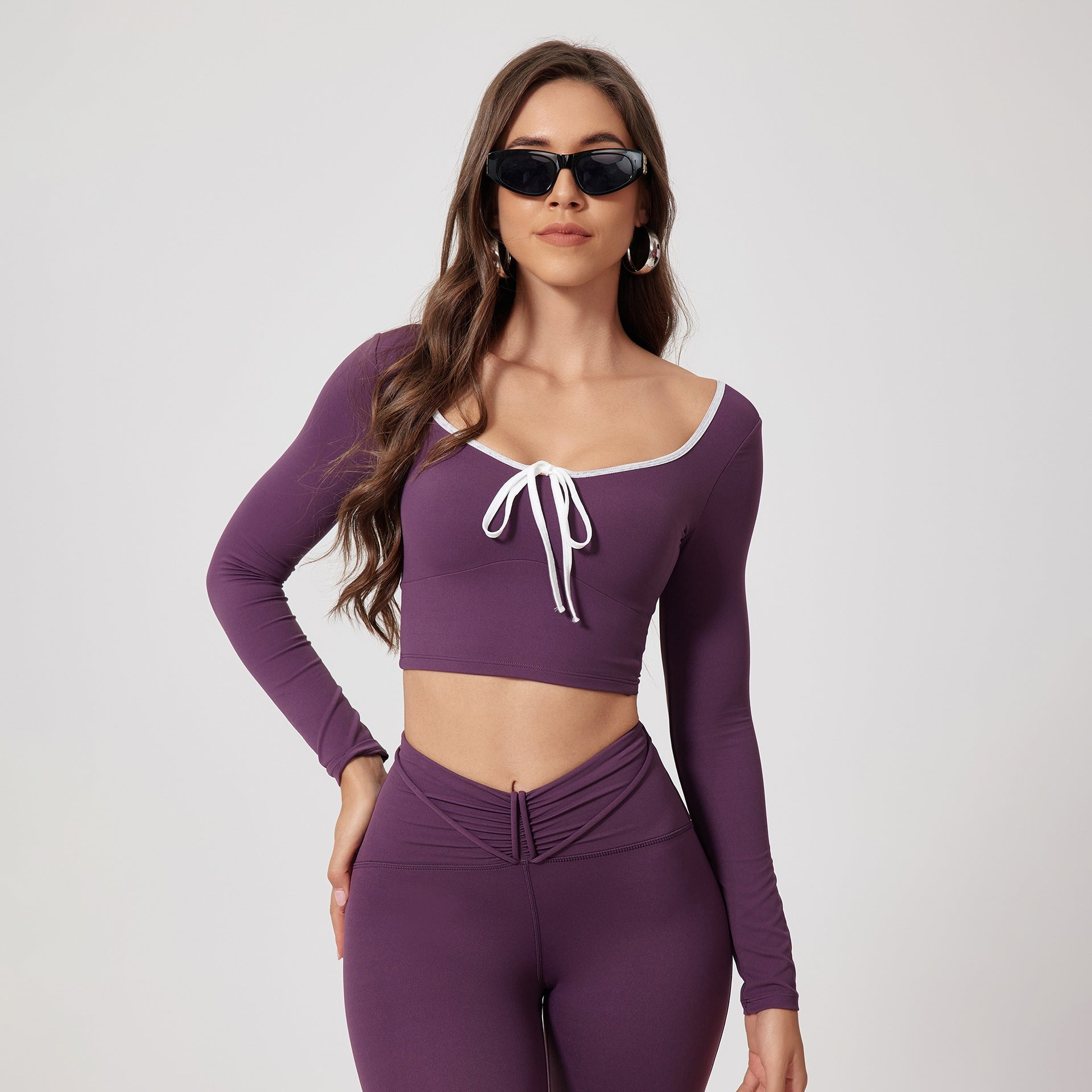 Purple athletic crop top and legging set modeled with trendy black sunglasses and silver hoop earrings, showcasing front tie and white trim details