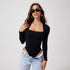 Model in black long-sleeve bodysuit with lace trim, sunglasses, and light jeans, standing against white background