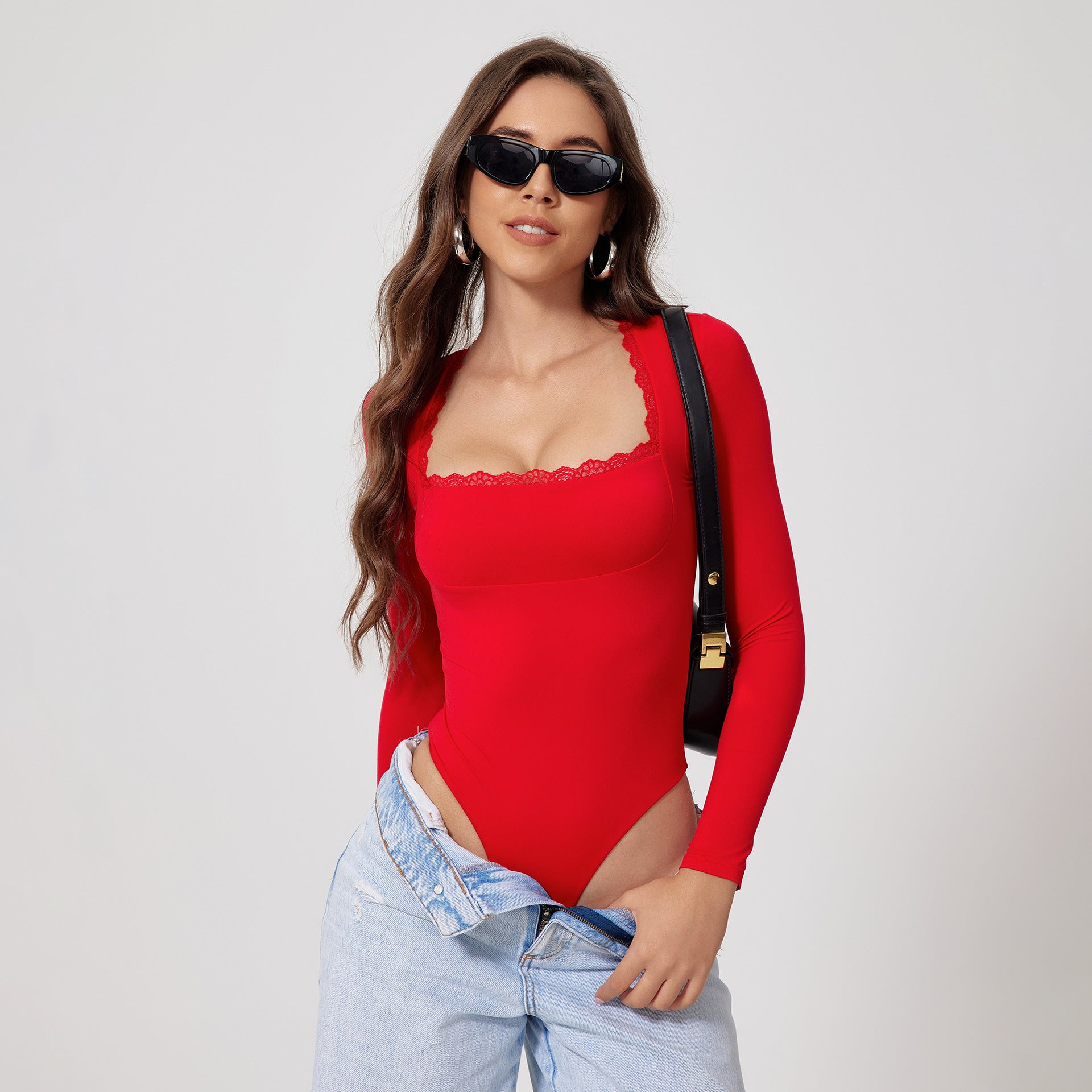 Model wearing red long-sleeve bodysuit with lace trim, sunglasses, black shoulder bag, and light jeans against white backdrop
