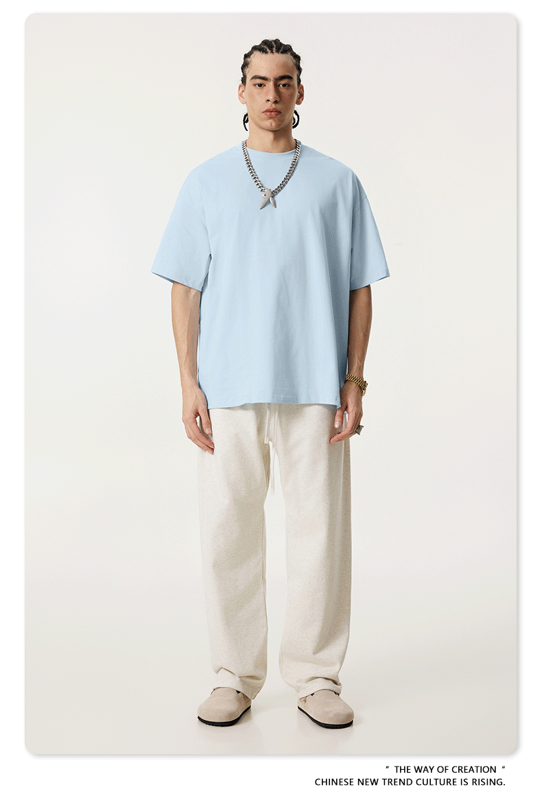 Model in light blue oversized t-shirt paired with cream drawstring pants and beige shoes, accessorized with silver chain necklace