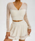 A model is wearing a cream mesh-sleeve crop top with V-neckline and matching flared mini skirt with sheer panel detail, posed against a light background