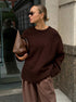 A model is posing in a chocolate brown knit sweater with matching trousers against stone building. Hair in sleek bun with small sunglasses