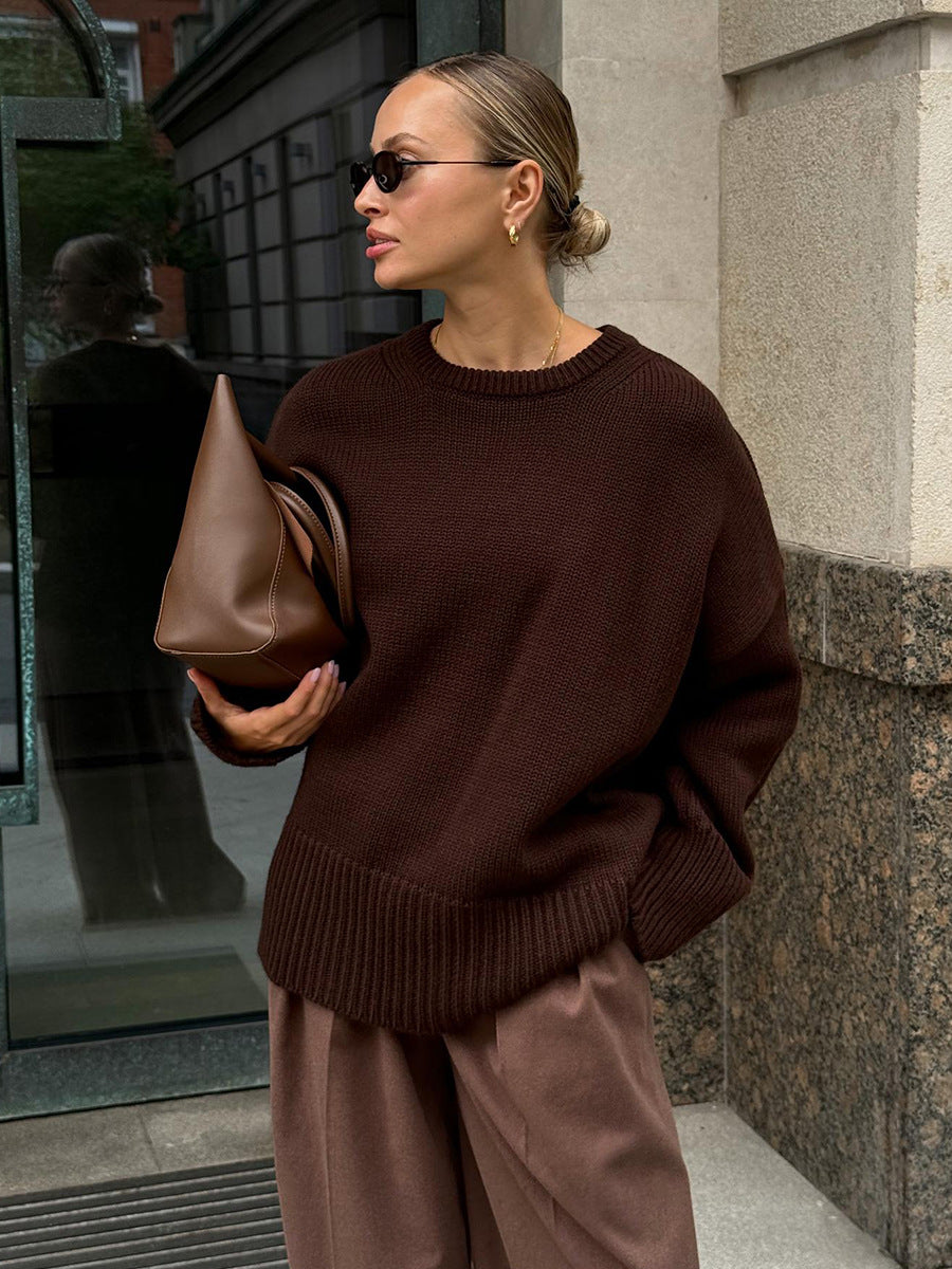 A model is posing in a chocolate brown knit sweater with matching trousers against stone building. Hair in sleek bun with small sunglasses